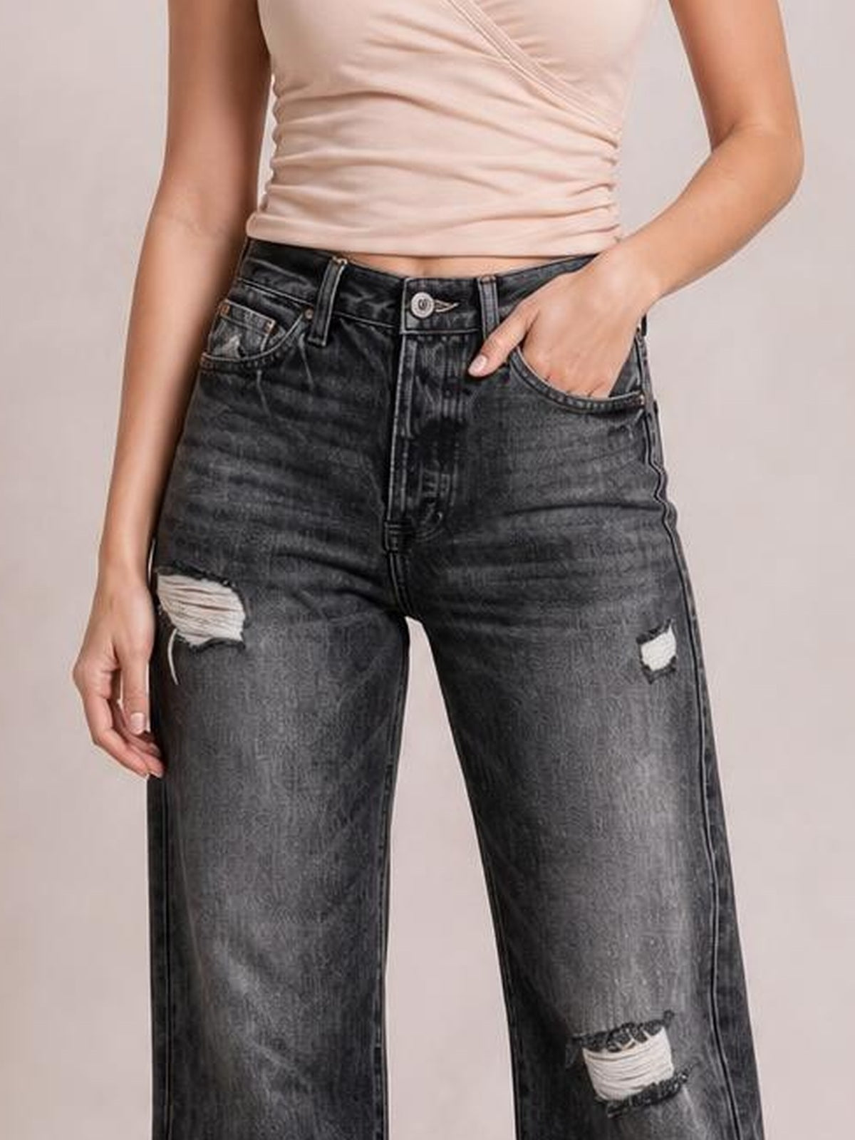 Model wears dark gray distressed straight-leg jeans with ripped knees and thigh, belt loops, five-pocket styling, and one hand in a pocket.