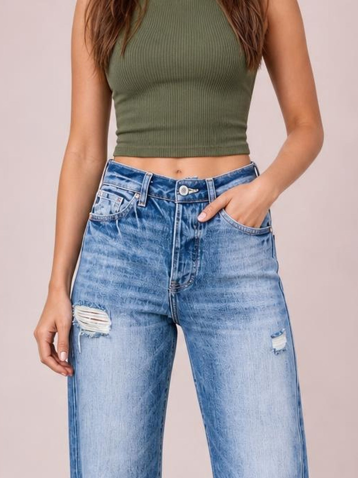 A model wears light blue distressed straight-leg jeans with ripped thigh details, belt loops, front pockets, and a button fly, posing with one hand in a pocket.