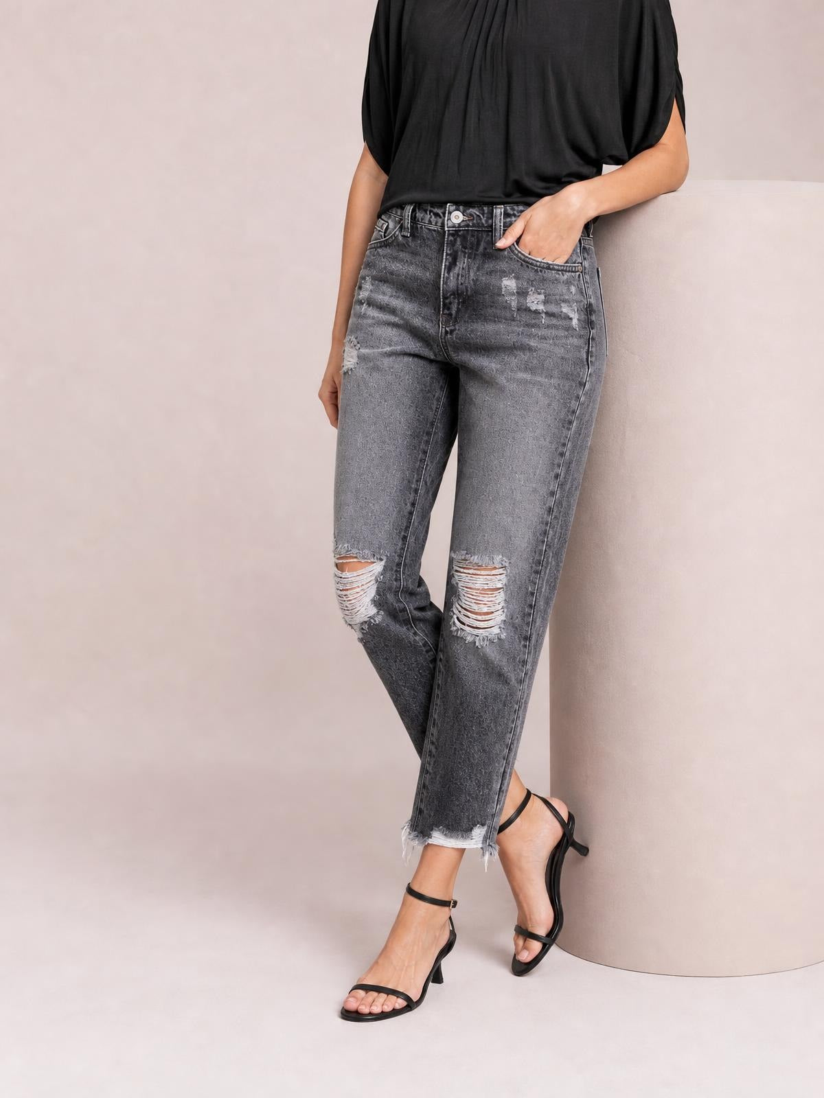 Model poses in distressed gray ankle jeans with a straight-leg silhouette, ripped knees, five-pocket construction, and raw frayed hems.
