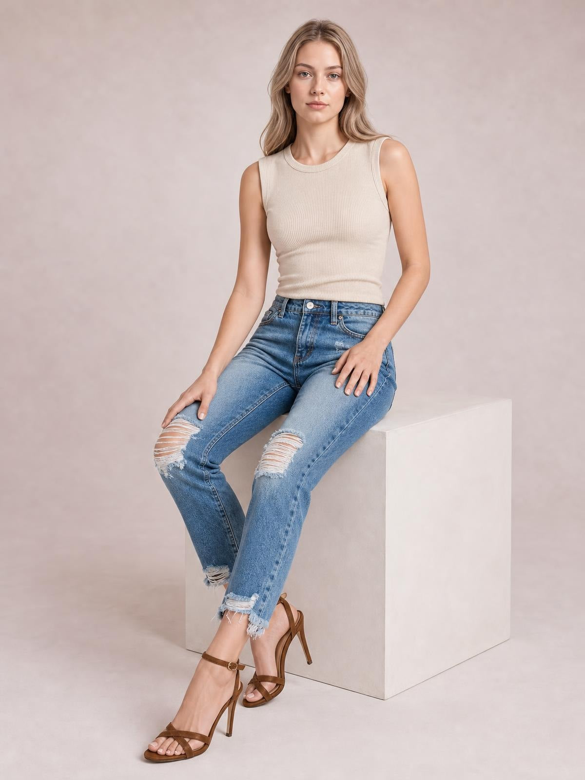 Seated model wears light-blue distressed wash ankle jeans with a high-rise five-pocket design, knee rips, straight legs, and frayed raw hems.