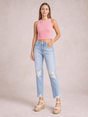 Model poses with one hand in the pocket of light-wash distressed ankle jeans featuring a straight-leg silhouette, ripped knees, and raw hems.