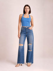 Model poses in blue distressed wide leg jeans with a button fly, pockets, frayed hems, and ripped knees and thighs.
