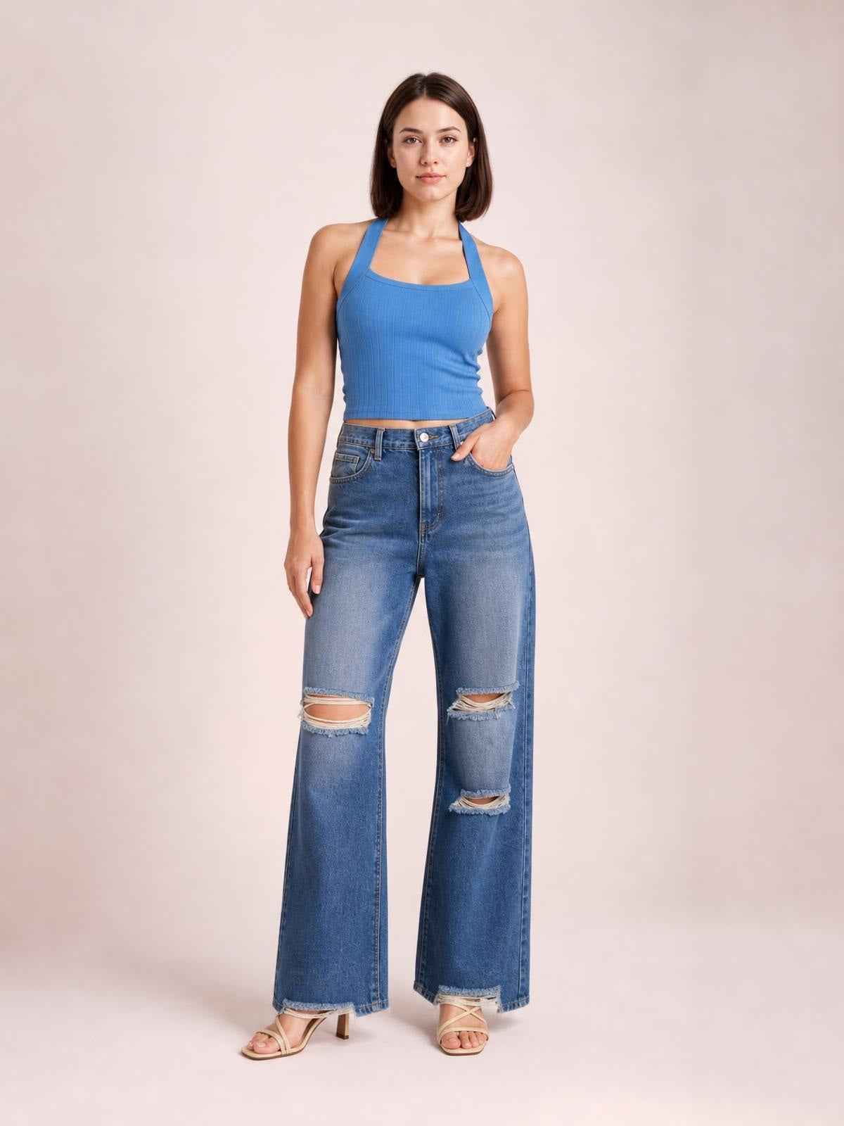 Model poses in blue distressed wide leg jeans with a button fly, pockets, frayed hems, and ripped knees and thighs.