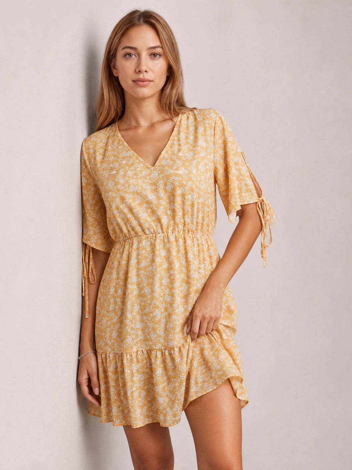 Model poses in a light yellow ditsy floral mini dress with a V-neck, tied half sleeves, softly gathered waist, and flounced hem.