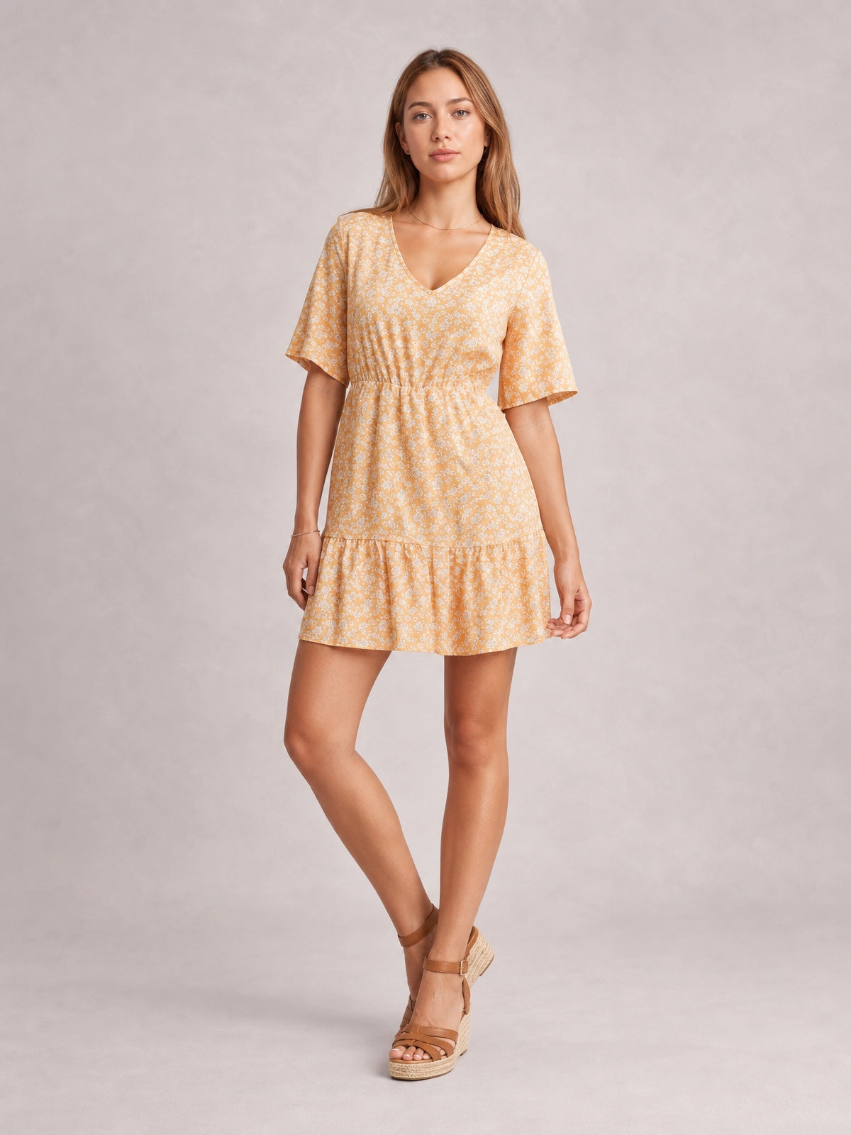 Model poses in a light yellow ditsy floral mini dress with a flattering V-neck, half sleeves, gathered waist, and flounced hem.
