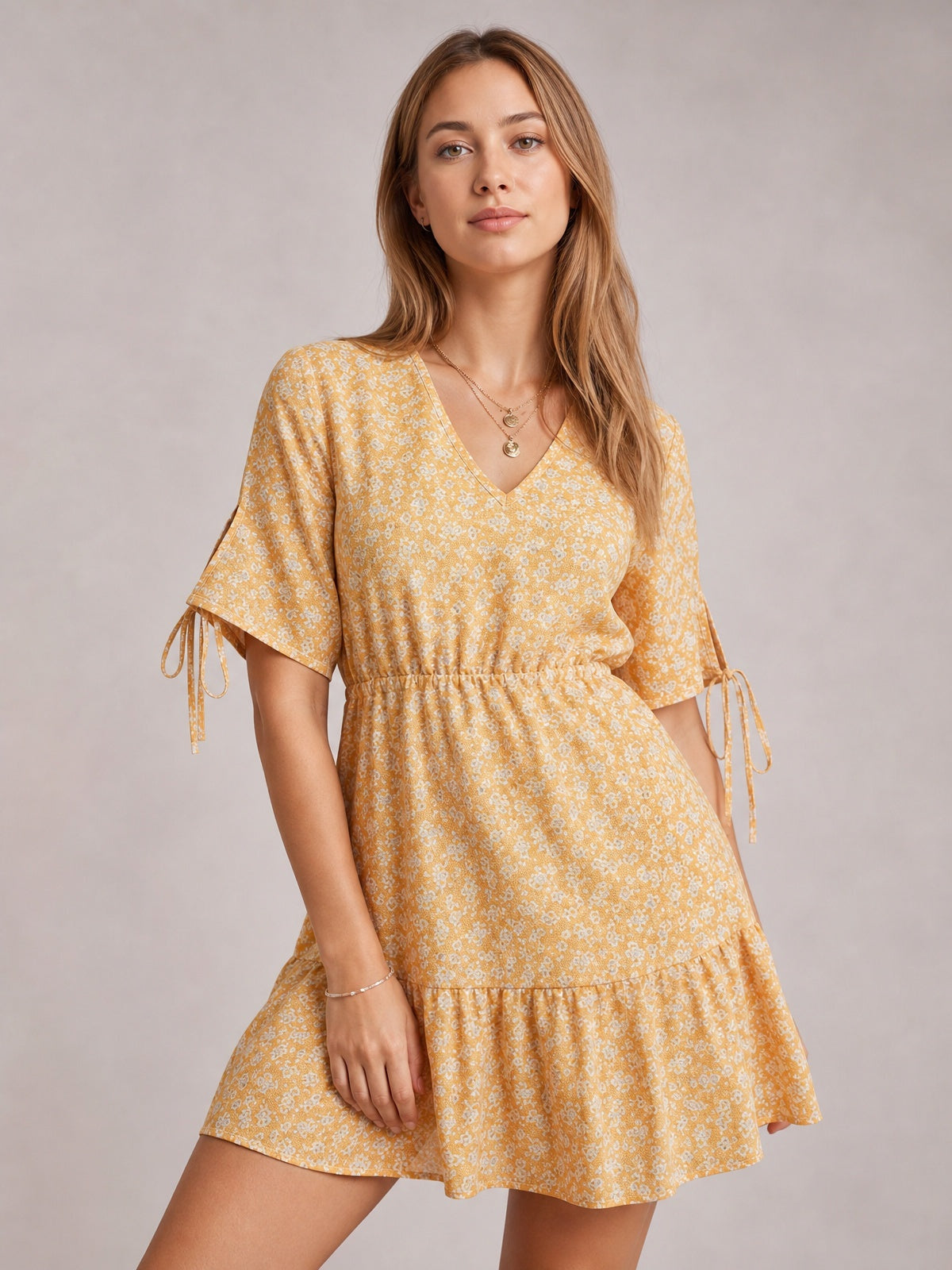 Model poses in a light yellow ditsy floral mini dress with a V-neck, tied half sleeves, defined gathered waist, and flounced hem.