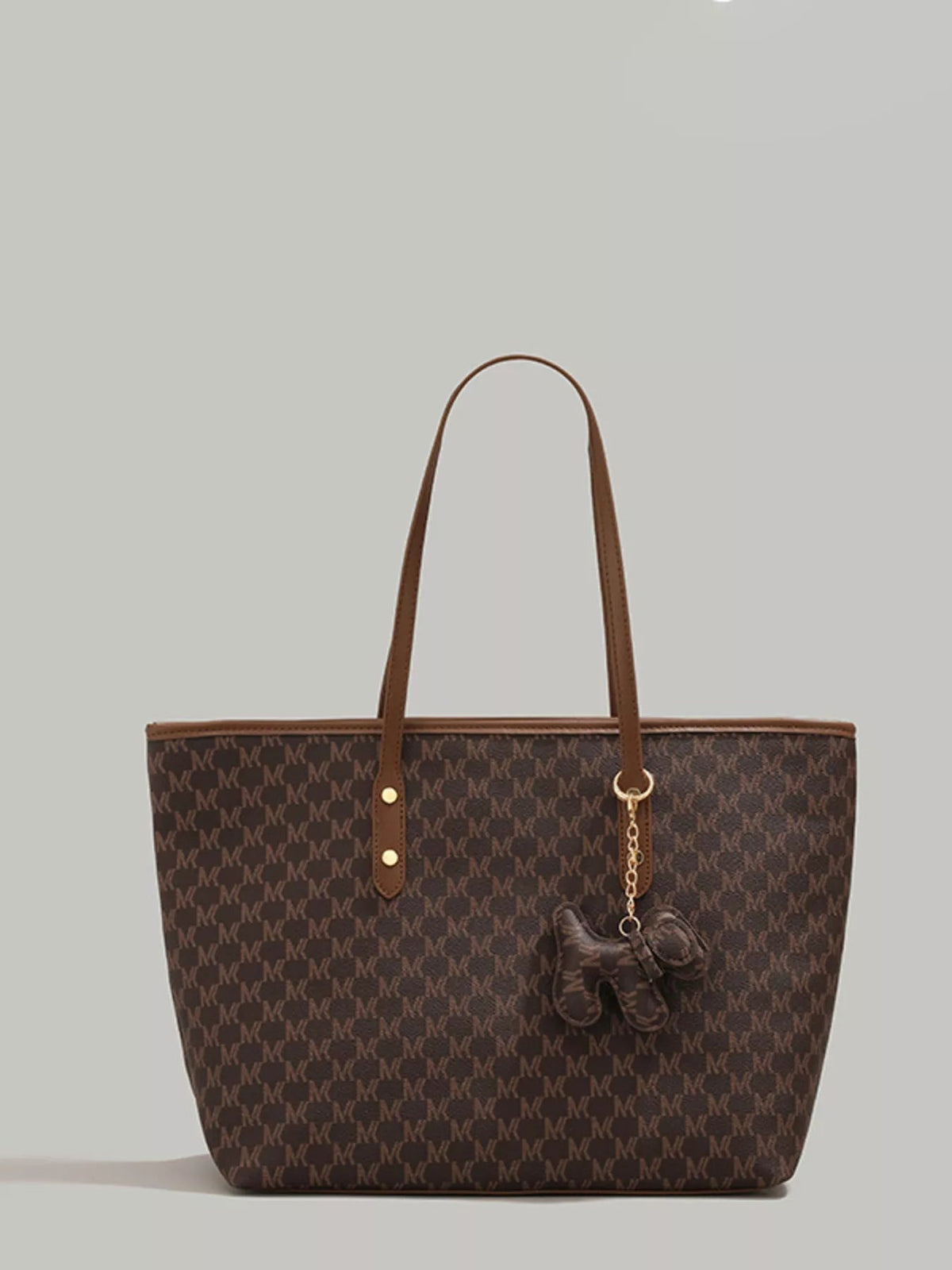 A large brown patterned PU leather tote bag with long shoulder handles, a structured silhouette, gold-tone hardware, and a dangling dog charm.