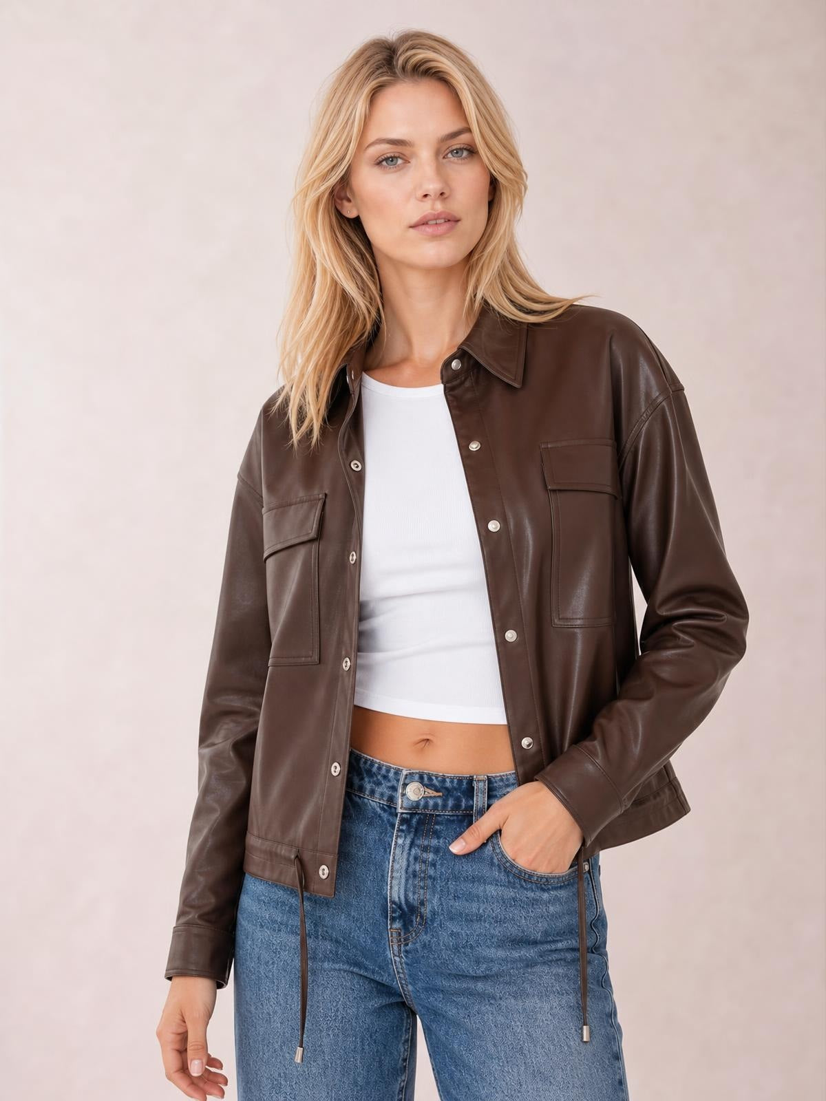 Model wears a brown leather jacket with button front, double flap pockets, long sleeves, a collared silhouette, and a drawstring hem.
