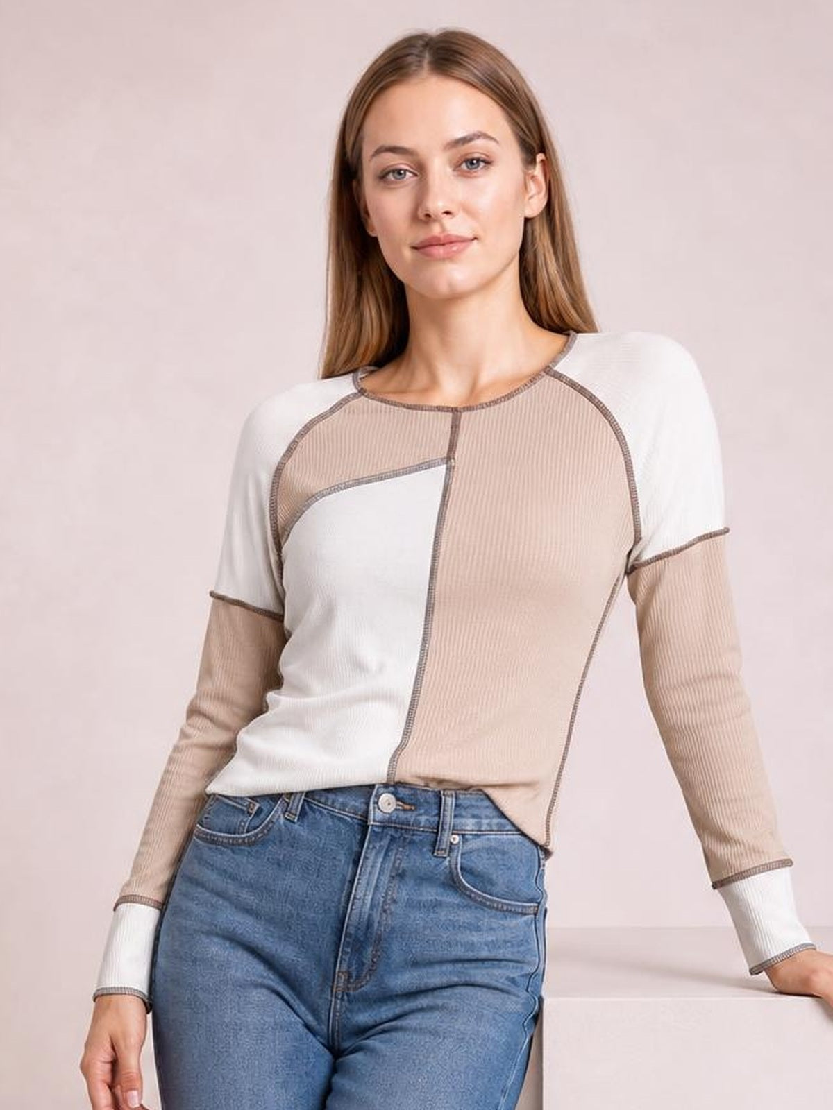 A model poses in a color block ribbed top with beige and white panels, long sleeves, a round neckline, and contrasting exposed seam detailing.
