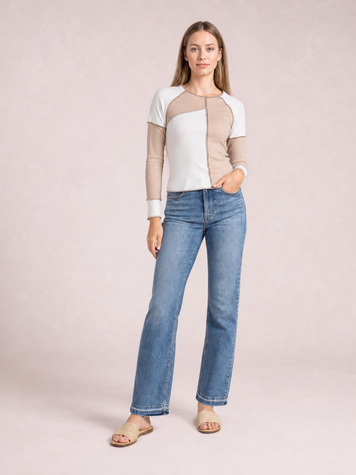 Model poses in a fitted ribbed color block top with beige and white panels, long sleeves, and visible exposed seams.