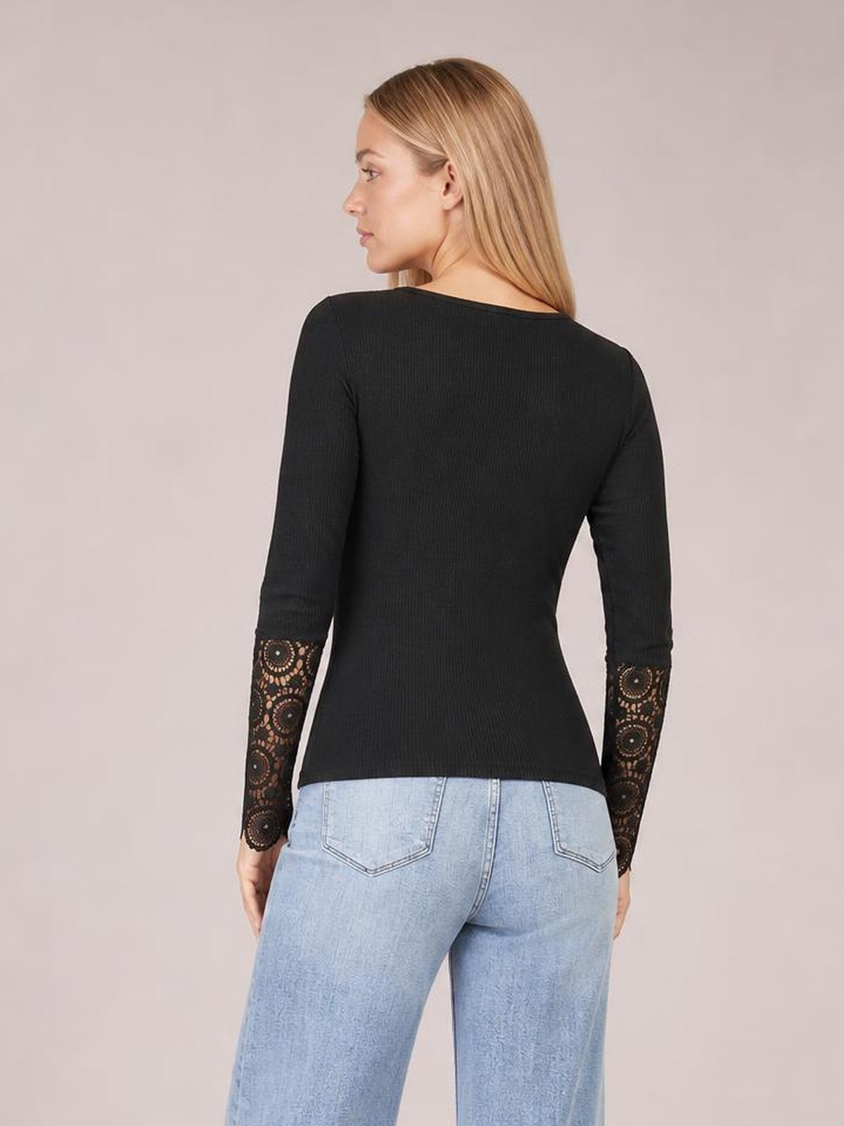 A model shown from behind wears a black fitted top with a solid ribbed body, long sleeves with crochet lace panels at the lower arms, and a straight hem.