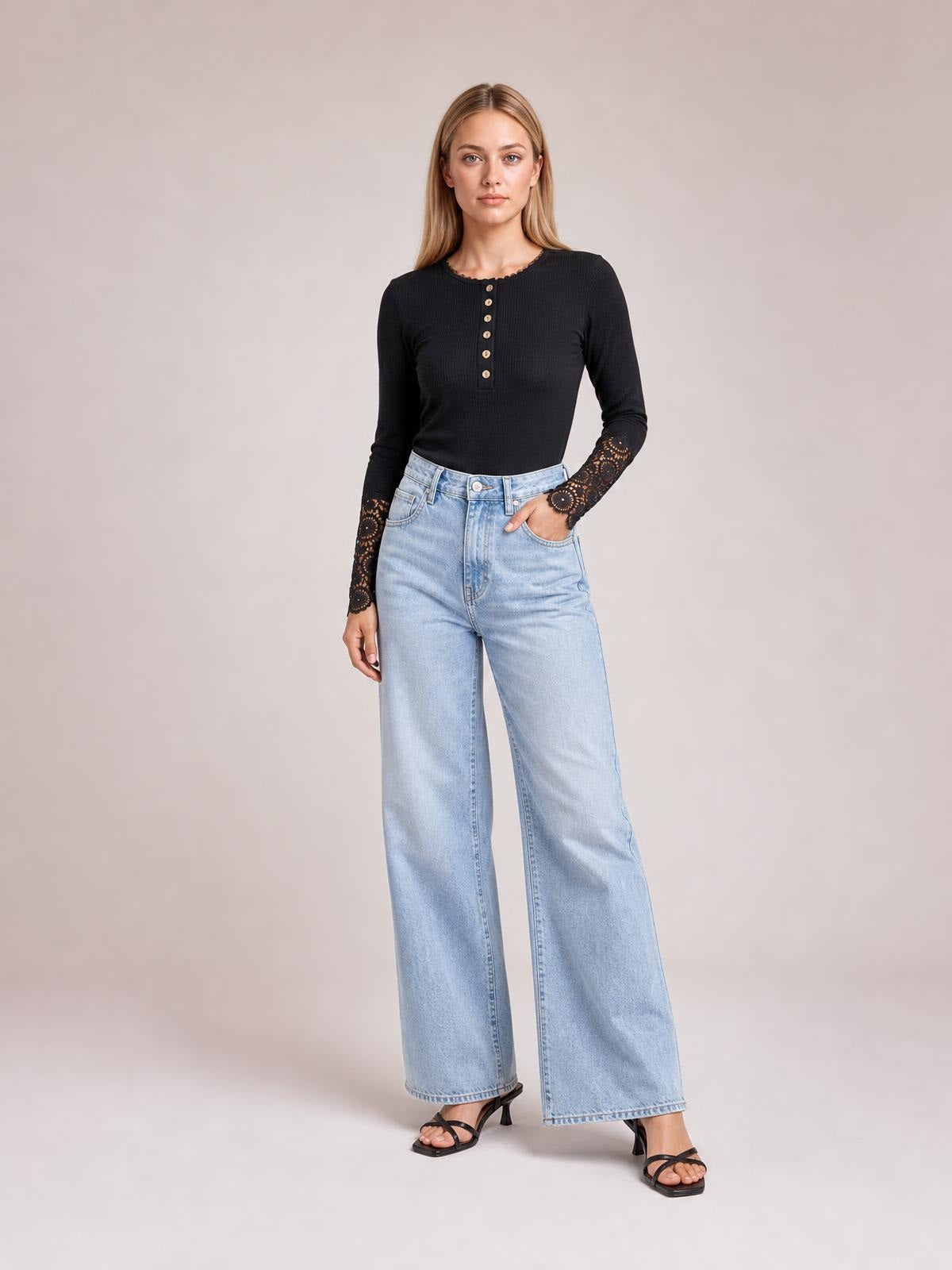 A model stands in a black button-front top with long sleeves, crochet lace cuffs, a fitted silhouette, and light-wash wide-leg jeans.