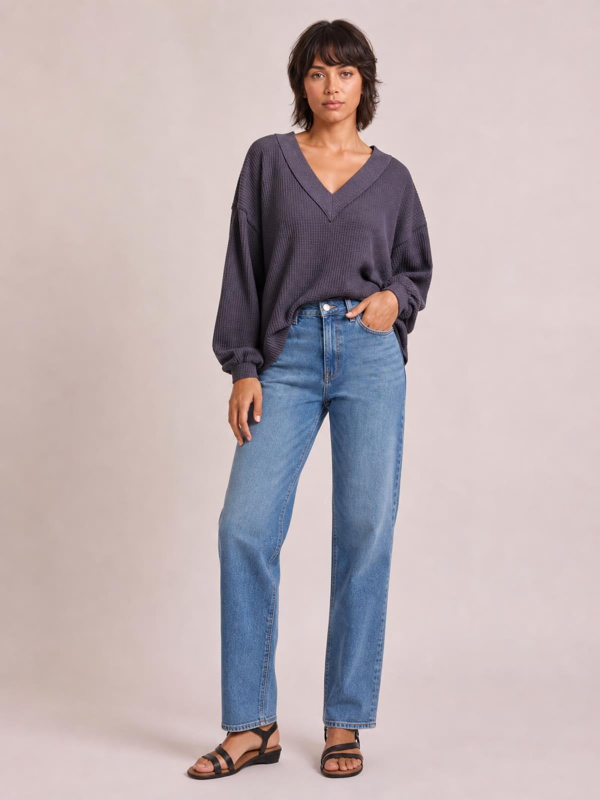 Model poses with one hand in her jeans pocket, wearing a charcoal ribbed textured V-neck long-sleeve T-shirt with exposed seams and a relaxed silhouette.