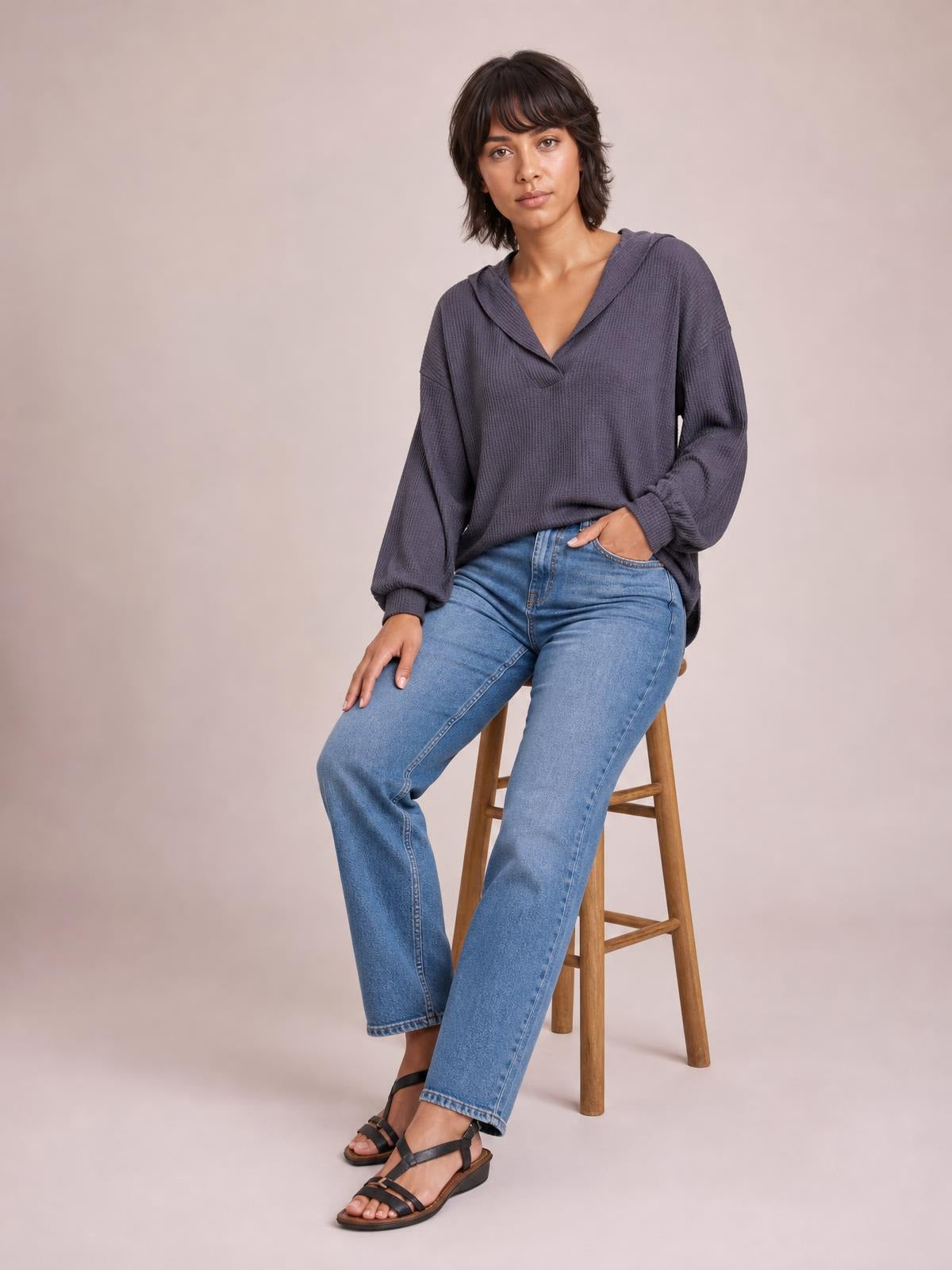 A model sits in a relaxed-fit charcoal ribbed textured V-neck long sleeve T-shirt with exposed seams, dropped shoulders, and gathered cuffs.