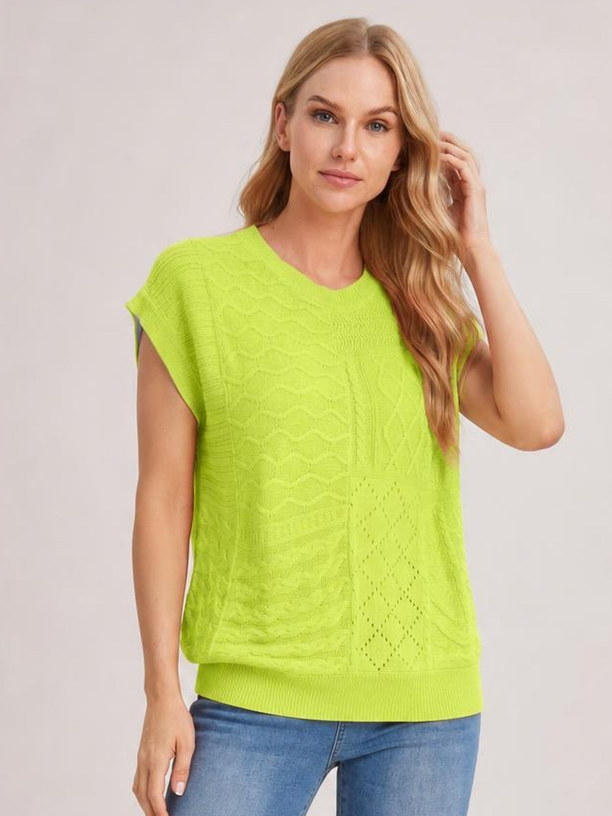 Model wearing a bright lime green cable-knit round neck cap sleeve sweater with a relaxed silhouette, ribbed hem, and textured panel construction.