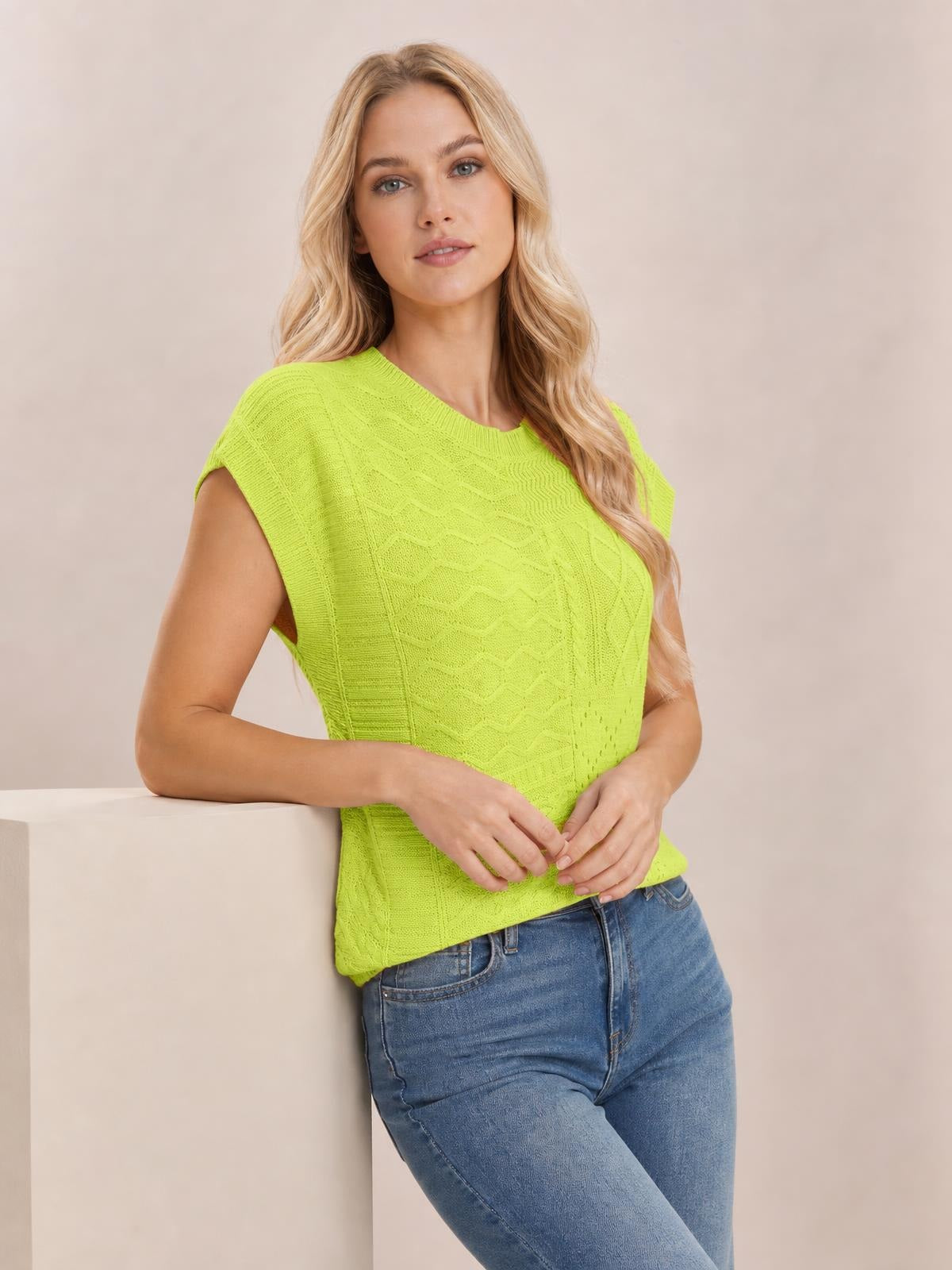 Model wearing a bright lime green cable-knit round neck cap sleeve sweater with a relaxed silhouette and textured vertical knit construction, hands resting at the waist.