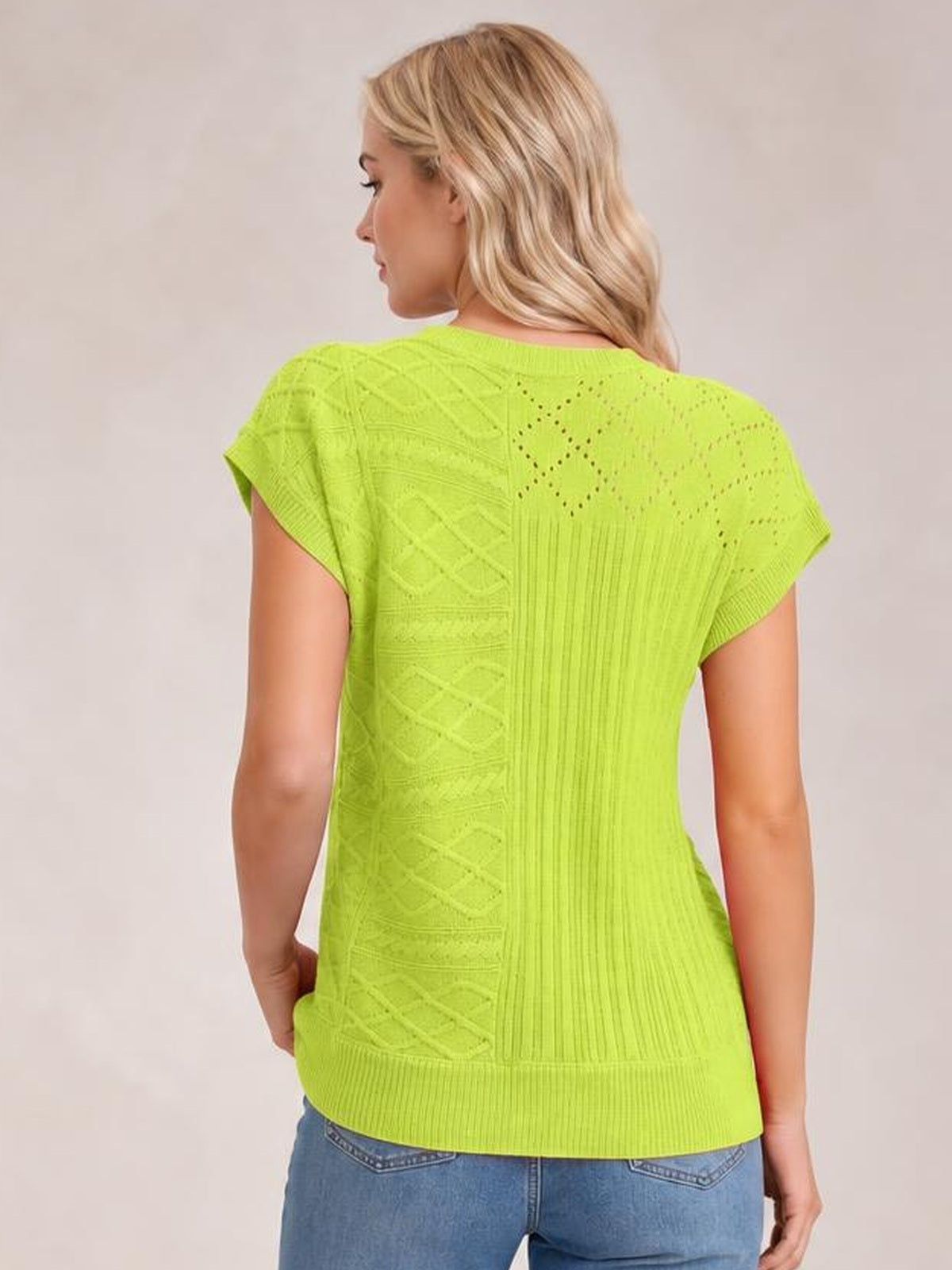 Back view of a model wearing a bright lime green cable-knit round neck cap sleeve sweater with a relaxed silhouette and ribbed hem.