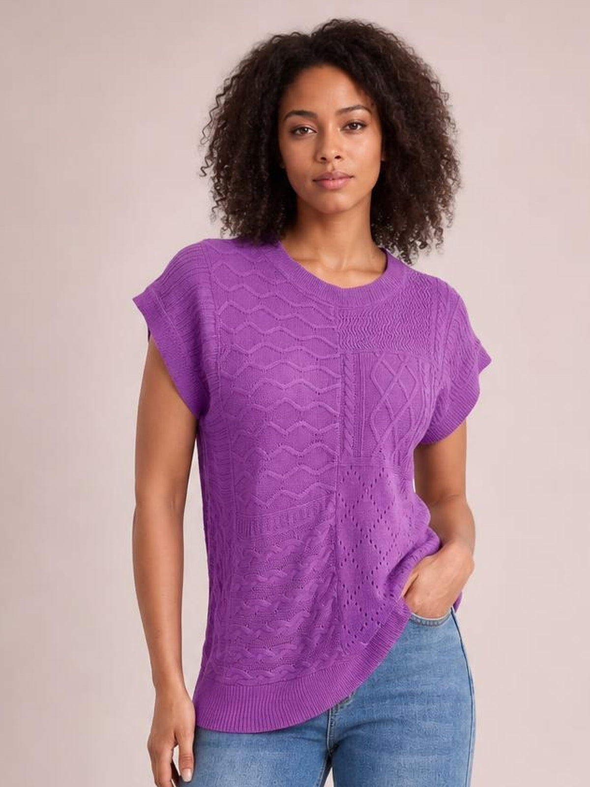 Model wearing a purple cable-knit round neck cap sleeve sweater with a relaxed silhouette, textured panel construction, and ribbed neckline and hem.