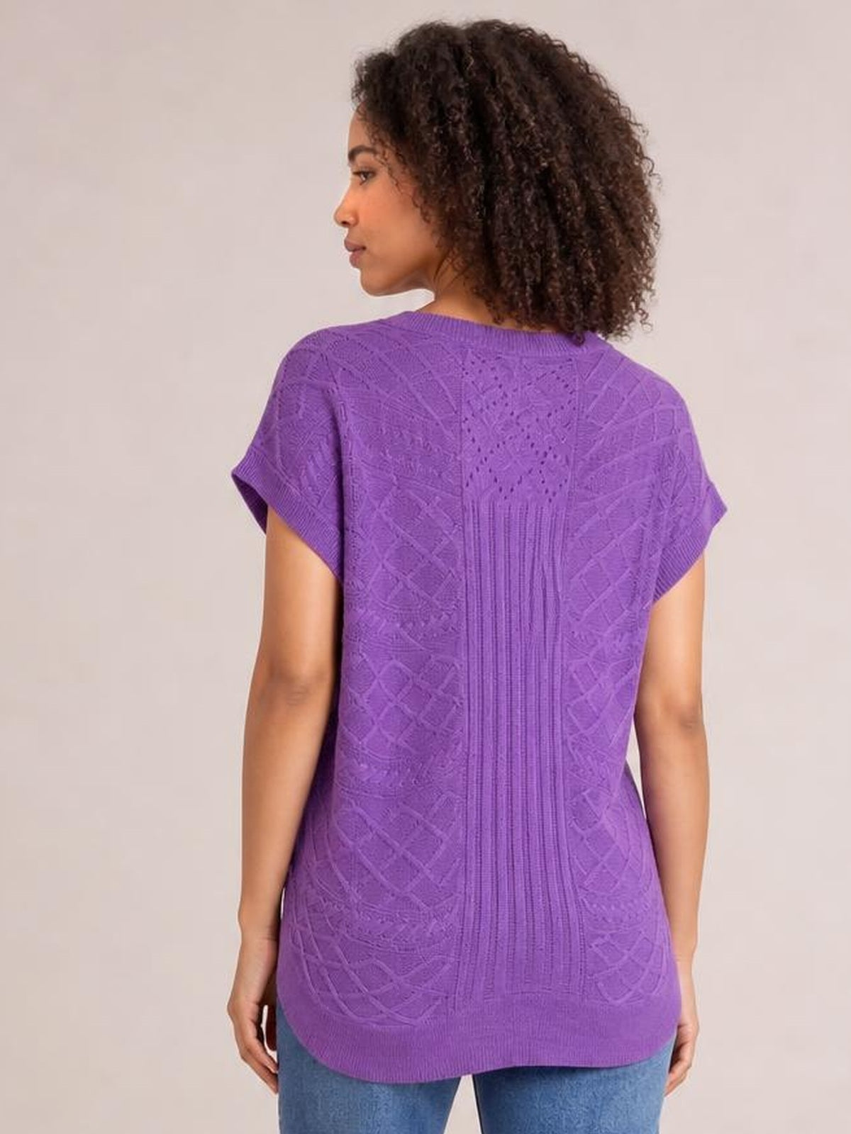 Model shown from the back wearing a purple cable-knit round neck cap sleeve sweater with a relaxed silhouette, ribbed trim, and textured knit panels.