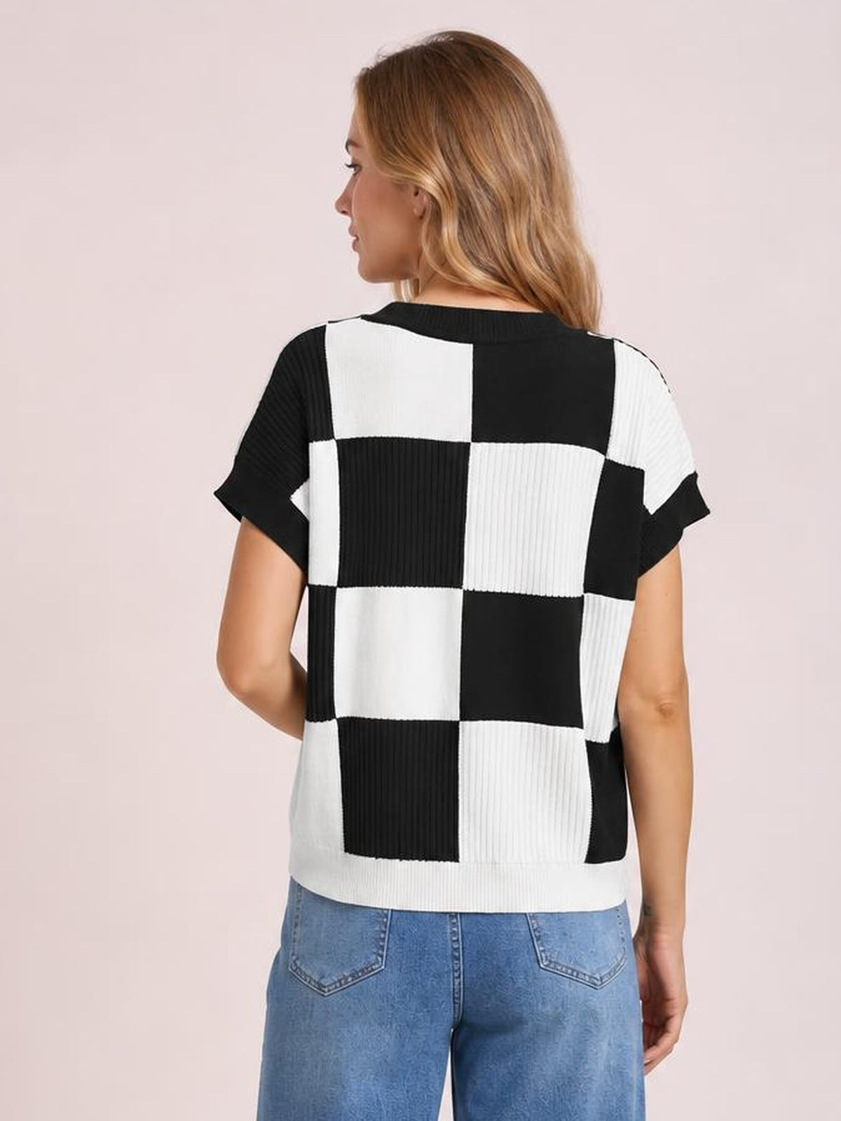 A model shows the back of a black-and-white checkered round neck short sleeve sweater with a relaxed silhouette and ribbed knit construction.