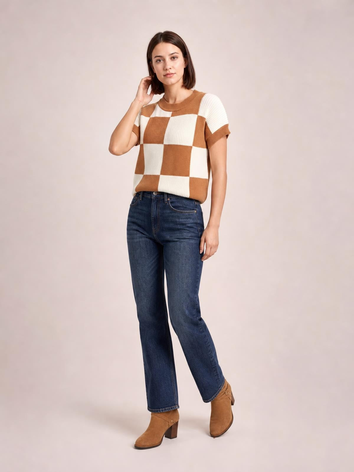 A model poses in a brown and cream checkered sweater with a round neck, short sleeves, ribbed trim, and a relaxed straight silhouette.