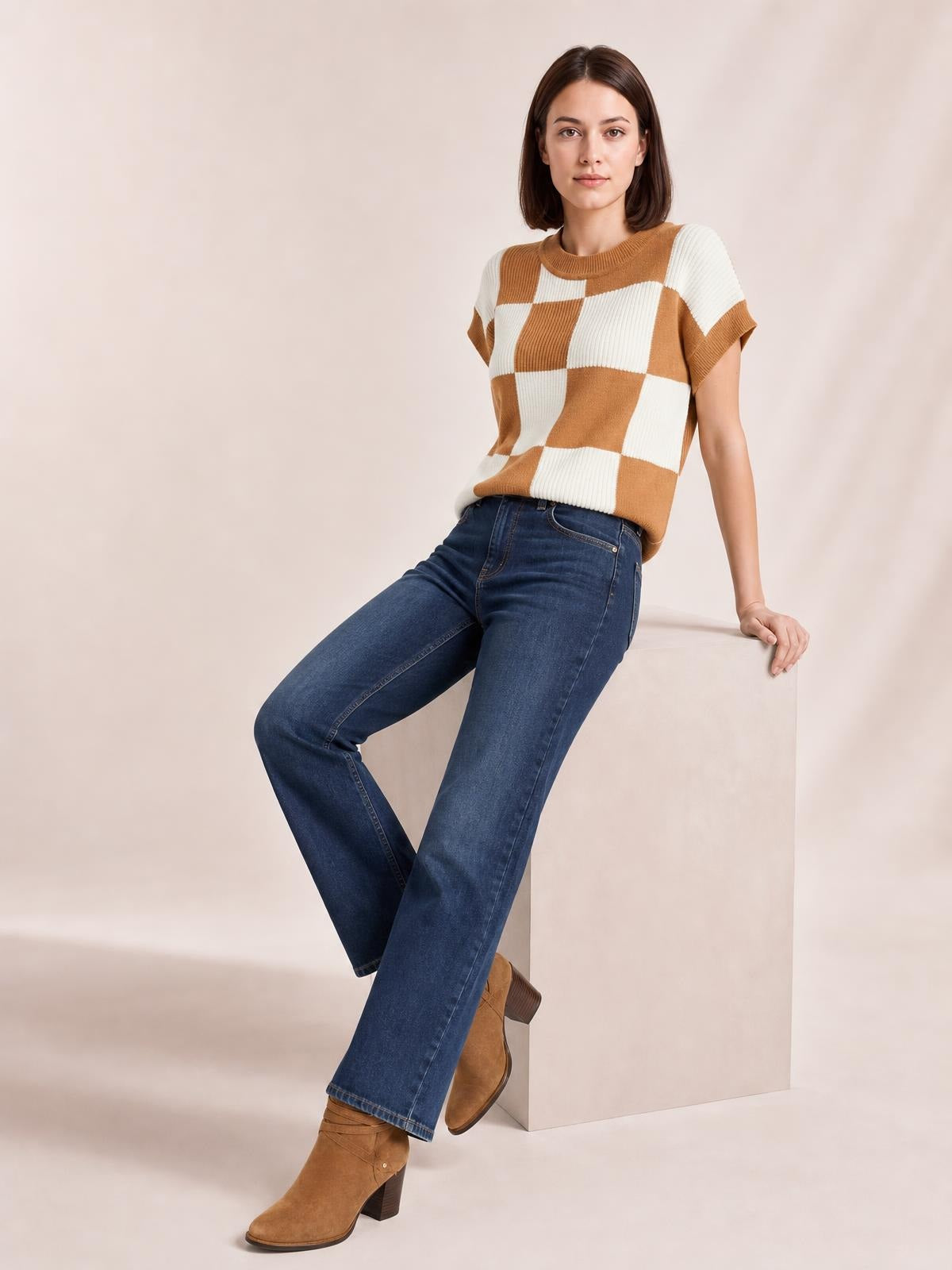 A woman leans against a pedestal wearing a camel and cream checkered round-neck short-sleeve sweater with a relaxed straight silhouette and ribbed trim.