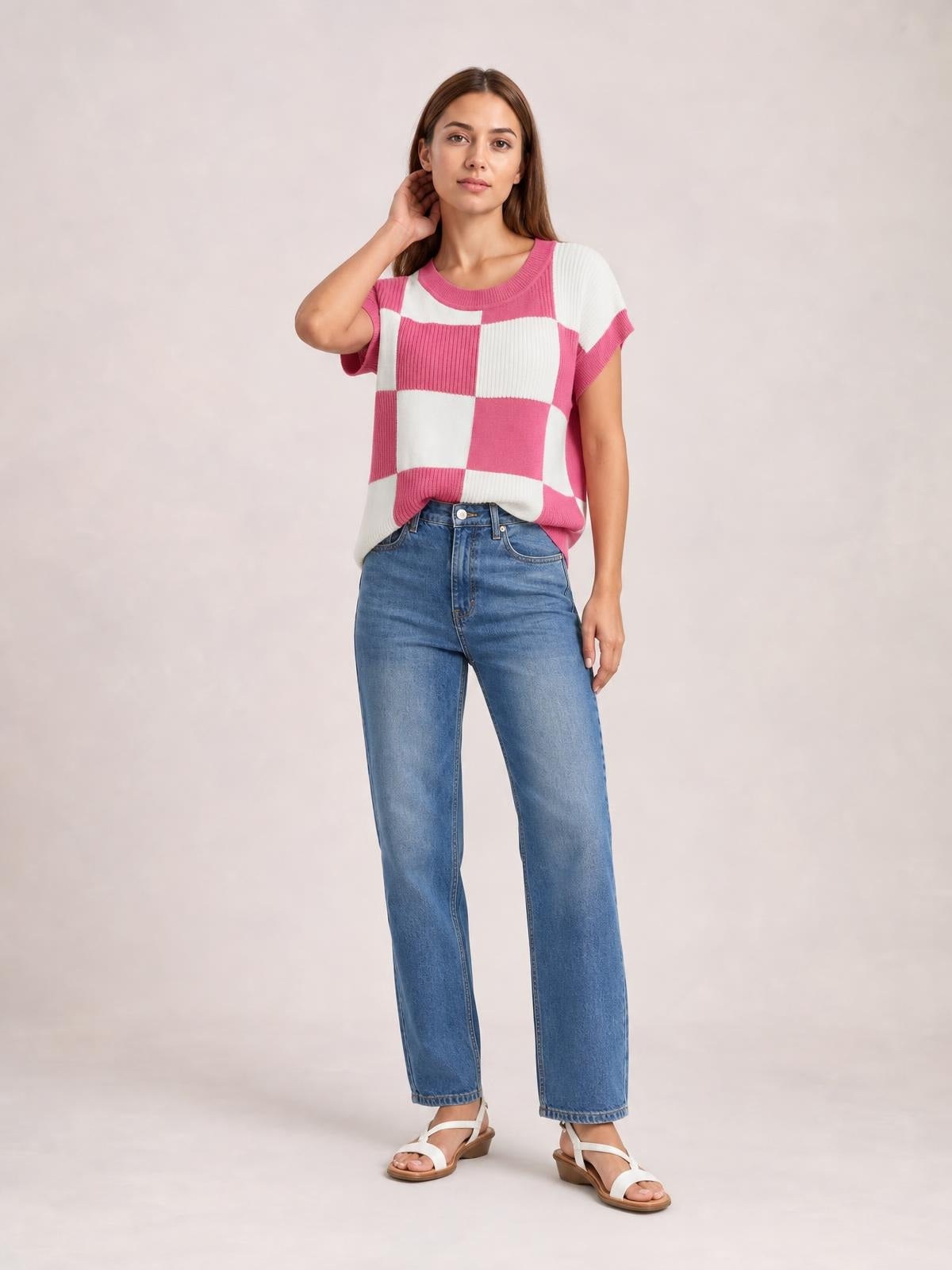Model wearing a pink and white checkered round neck short sleeve sweater with ribbed trim and a relaxed silhouette, posing with one hand near her neck.