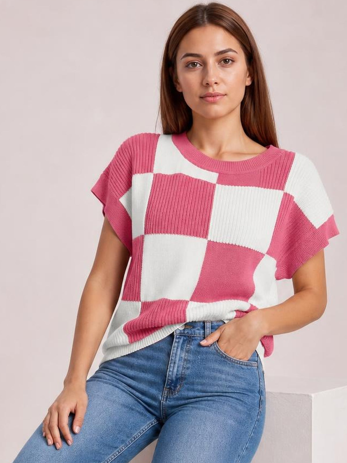 A model poses in a pink and white checkered round-neck short-sleeve sweater with a relaxed silhouette and ribbed knit construction.