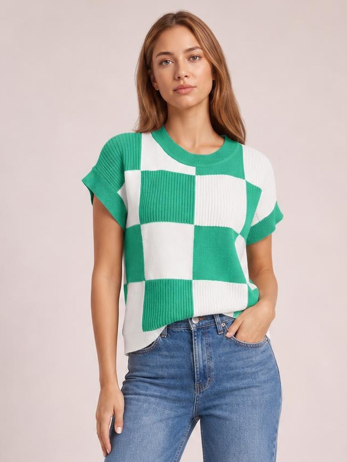 Model wears a green and white checkered round neck short sleeve sweater with ribbed construction, a relaxed straight silhouette, and one hand in her jeans pocket.