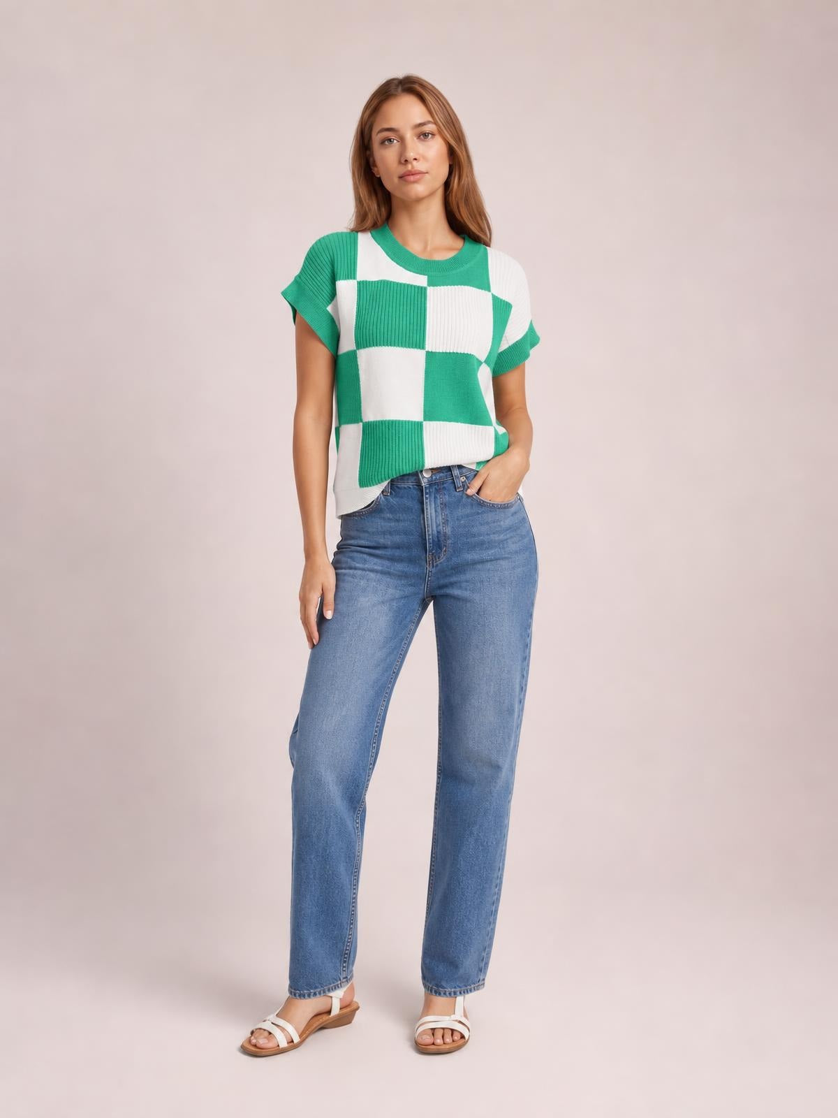 Model wearing a green and white checkered round neck short sleeve sweater with ribbed trim and a relaxed silhouette, posing with one hand in her jeans pocket.