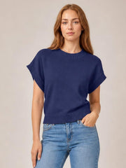 Model poses in a navy mock neck short sleeve sweater with a relaxed boxy silhouette, ribbed neckline, cuffs, and hem, paired with jeans.