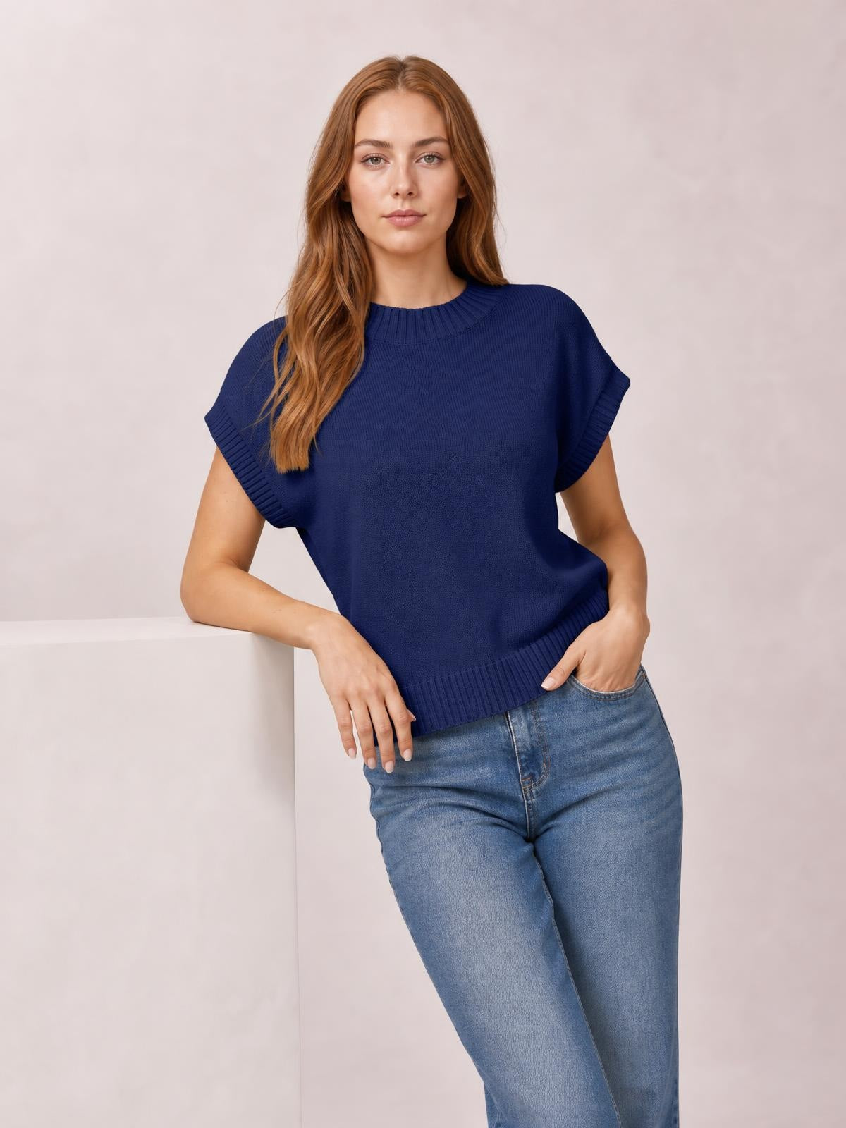 Model wears a navy mock neck short sleeve sweater with a relaxed silhouette, ribbed neckline, sleeve cuffs and hem, posing with hands in her jeans pockets.