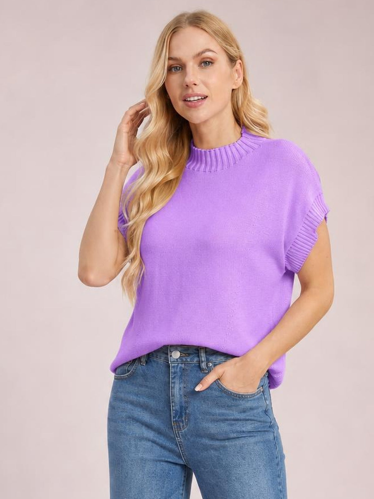 Model poses in a bright purple mock neck short sleeve sweater with ribbed neckline and sleeve cuffs, relaxed straight silhouette, and a tucked hem over jeans.