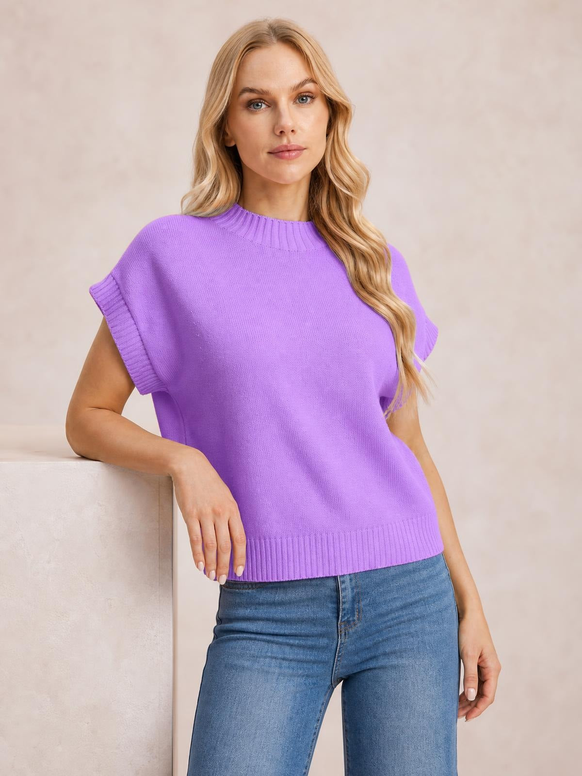 Model in a relaxed pose wears a purple mock neck short sleeve sweater with a loose silhouette, ribbed neckline, cuffs, and hem.