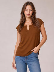 Model wears a brown notched cap sleeve knit top with a relaxed straight silhouette and ribbed hem, posing with one hand in her jeans pocket.