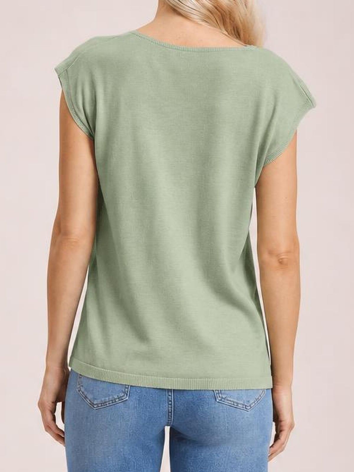 A model stands with arms at her sides wearing a sage green knit top with cap sleeves, a relaxed silhouette, and ribbed neckline and hem trim.