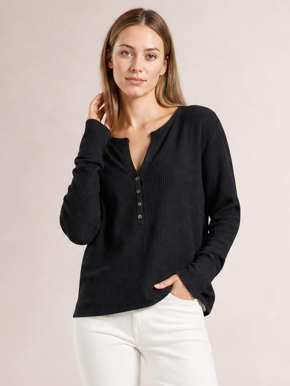 Model wears a black notched thumbhole long sleeve T-shirt with a relaxed silhouette, ribbed texture, buttoned front, and curved hem.