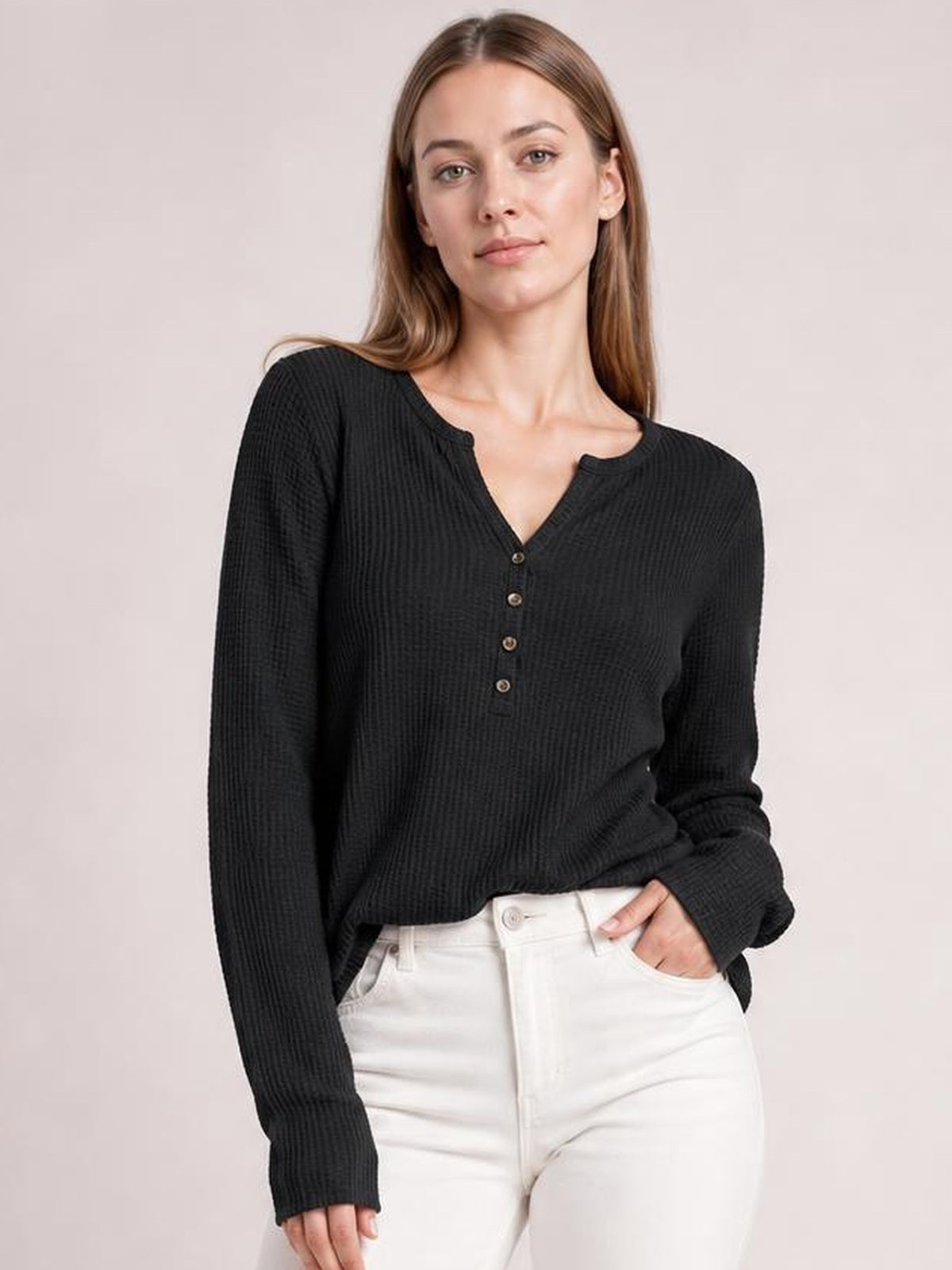 A model wears a black ribbed notched thumbhole long sleeve T-shirt with a buttoned neckline and relaxed silhouette, one hand in her pocket.