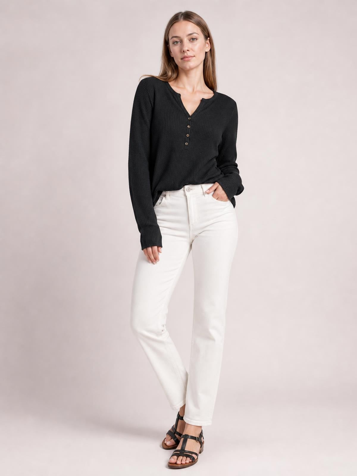 Model wears a black notched thumbhole long sleeve T-shirt with a relaxed silhouette, ribbed texture, and button details, standing with one hand in her pocket.