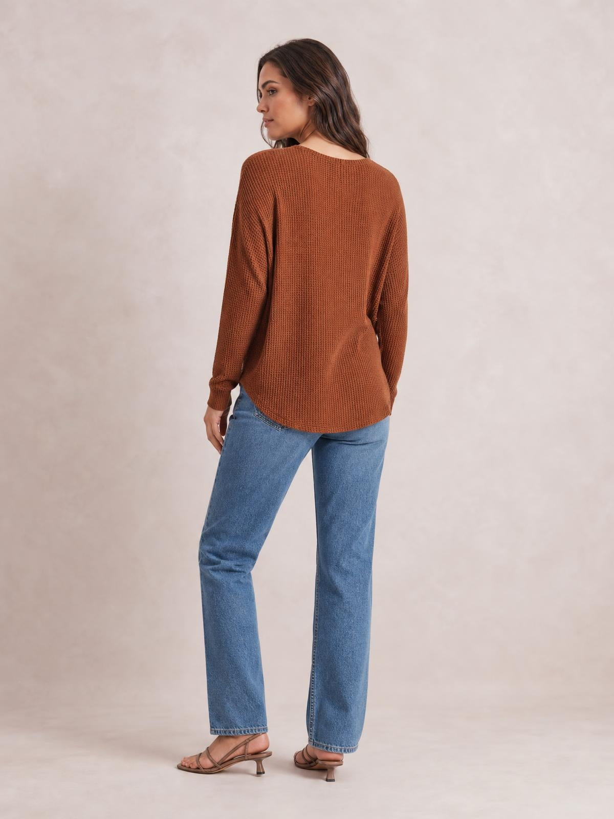 Model shown from the back wears a rust-brown notched long sleeve T-shirt with a relaxed silhouette, textured knit, curved hem, and fitted cuffs.