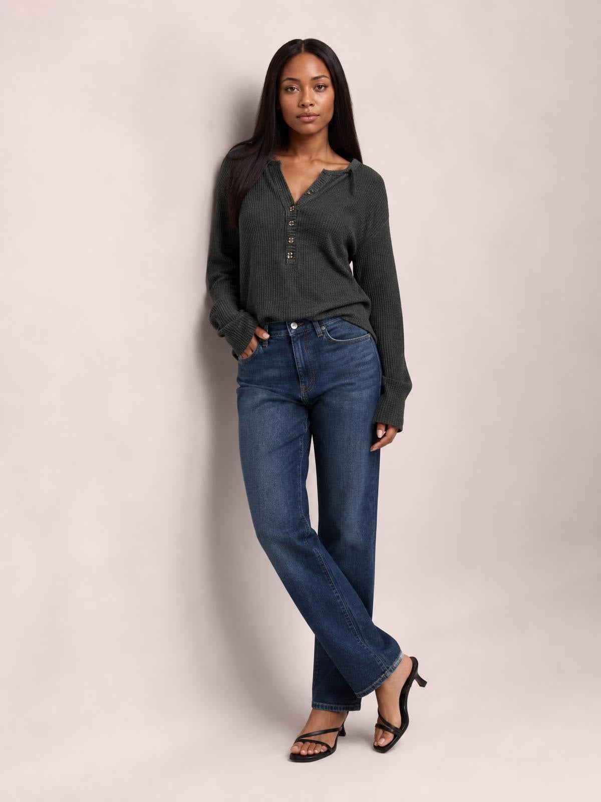Model wears a charcoal long-sleeve T-shirt with a notched neckline, button placket, textured knit, and relaxed silhouette while posing with one hand in her jeans pocket.