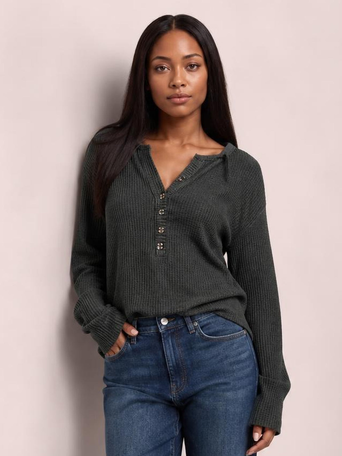 A model wears a charcoal notched long sleeve T-shirt with a textured knit, buttoned neckline, relaxed silhouette, and one hand tucked into her jeans pocket.