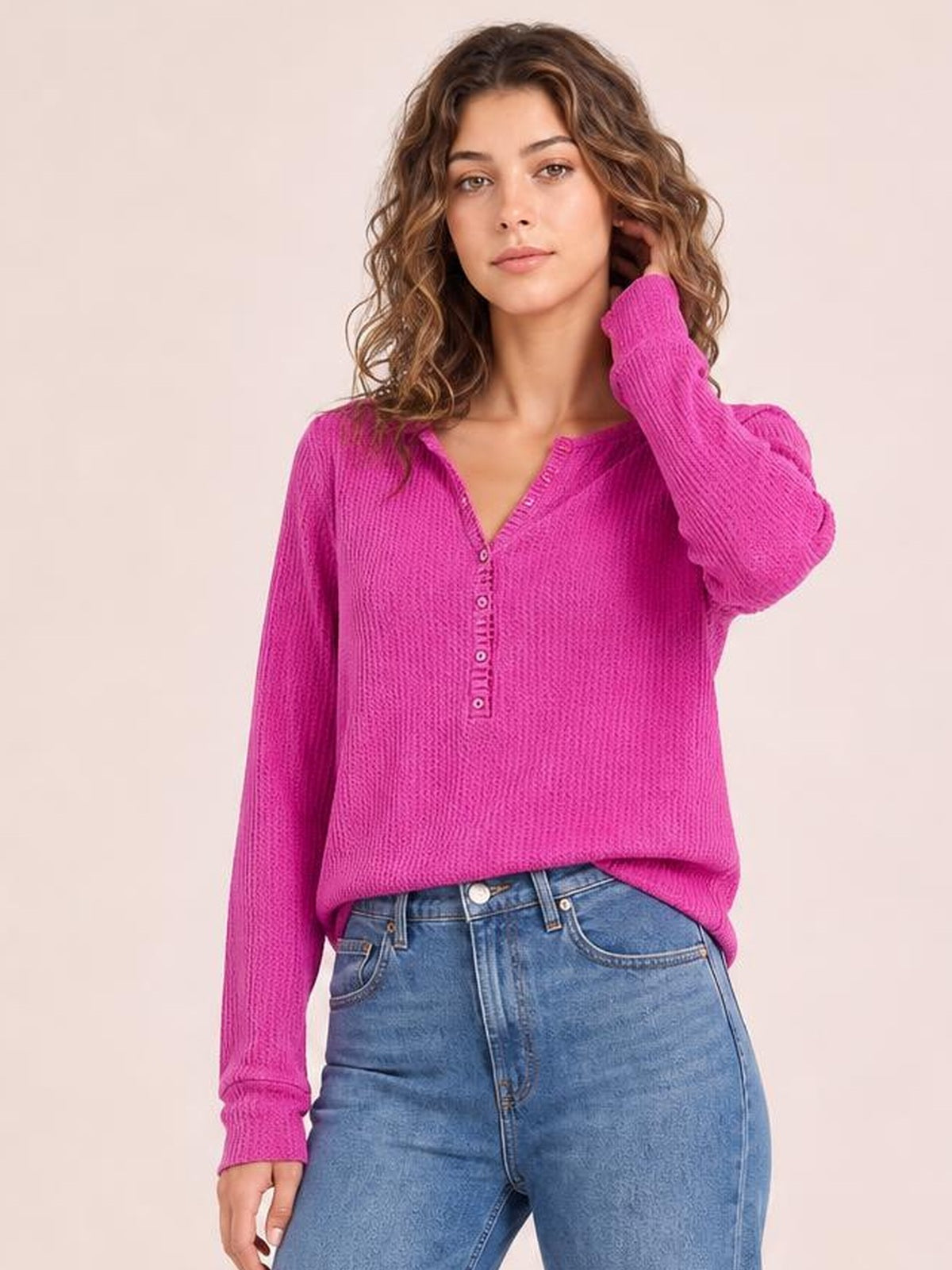 A model poses in a relaxed magenta long-sleeve T-shirt with a notched neckline, button placket, ribbed texture, and gently loose silhouette.