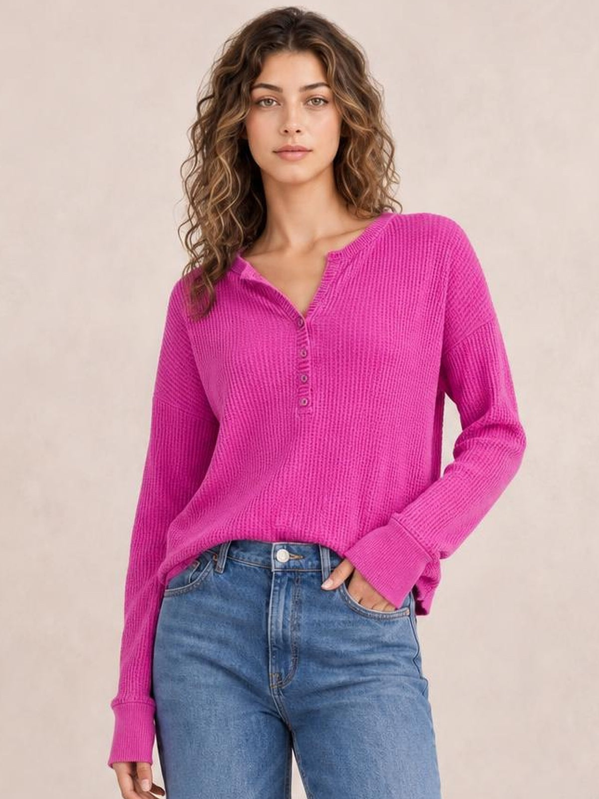 A model wears a bright pink notched long sleeve T-shirt with a ribbed texture, V-neckline, button placket, relaxed silhouette, and extended cuffs.