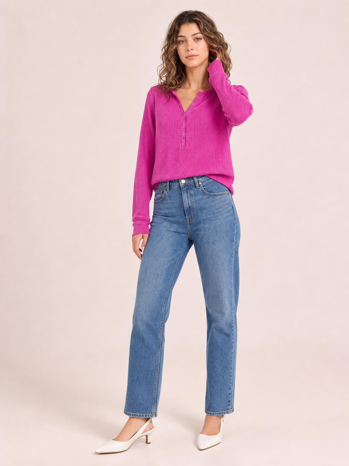 Model poses in a bright fuchsia notched long sleeve T-shirt with a relaxed silhouette, V-neck, button placket, and textured construction, touching her hair.