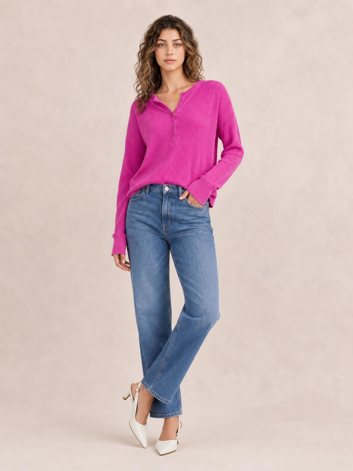 A model poses in a bright pink notched long sleeve T-shirt with a button placket, ribbed texture, relaxed silhouette, and extended cuffs, one hand in her pocket.