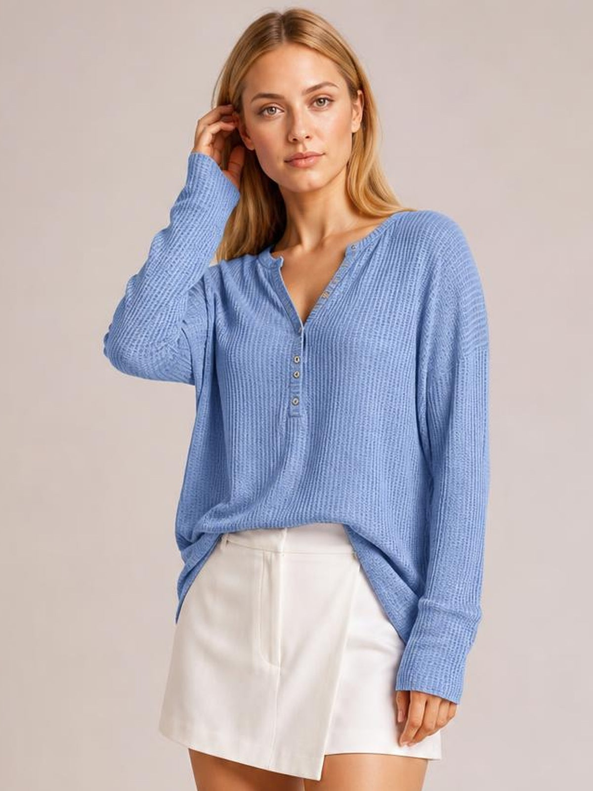 A model poses in a relaxed blue long-sleeve T-shirt with a notched neckline, button placket, textured fabric, and loose silhouette.