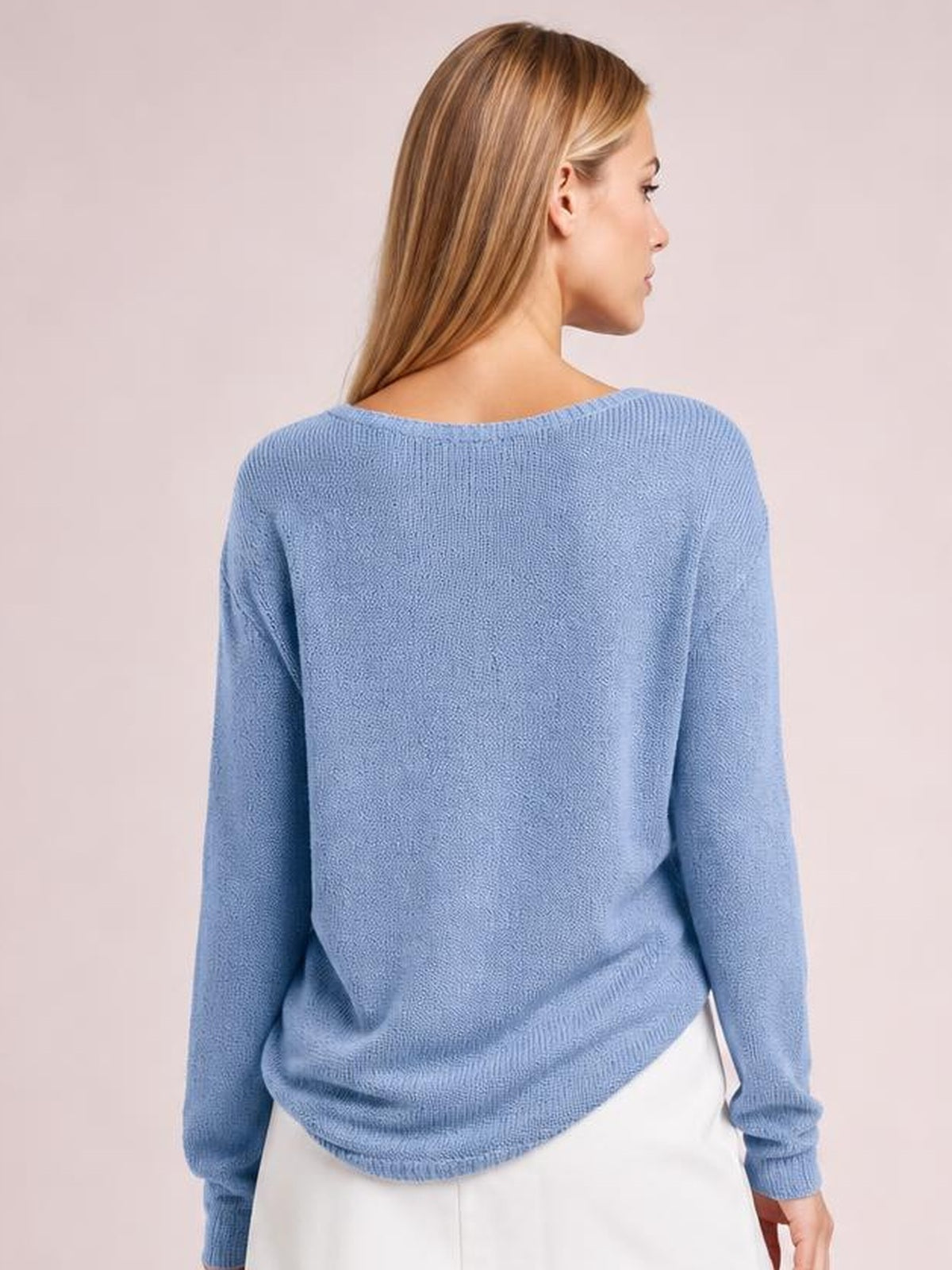 A model faces away wearing a light blue long-sleeve top with a relaxed silhouette, wide neckline, textured knit construction, and ribbed cuffs and hem.