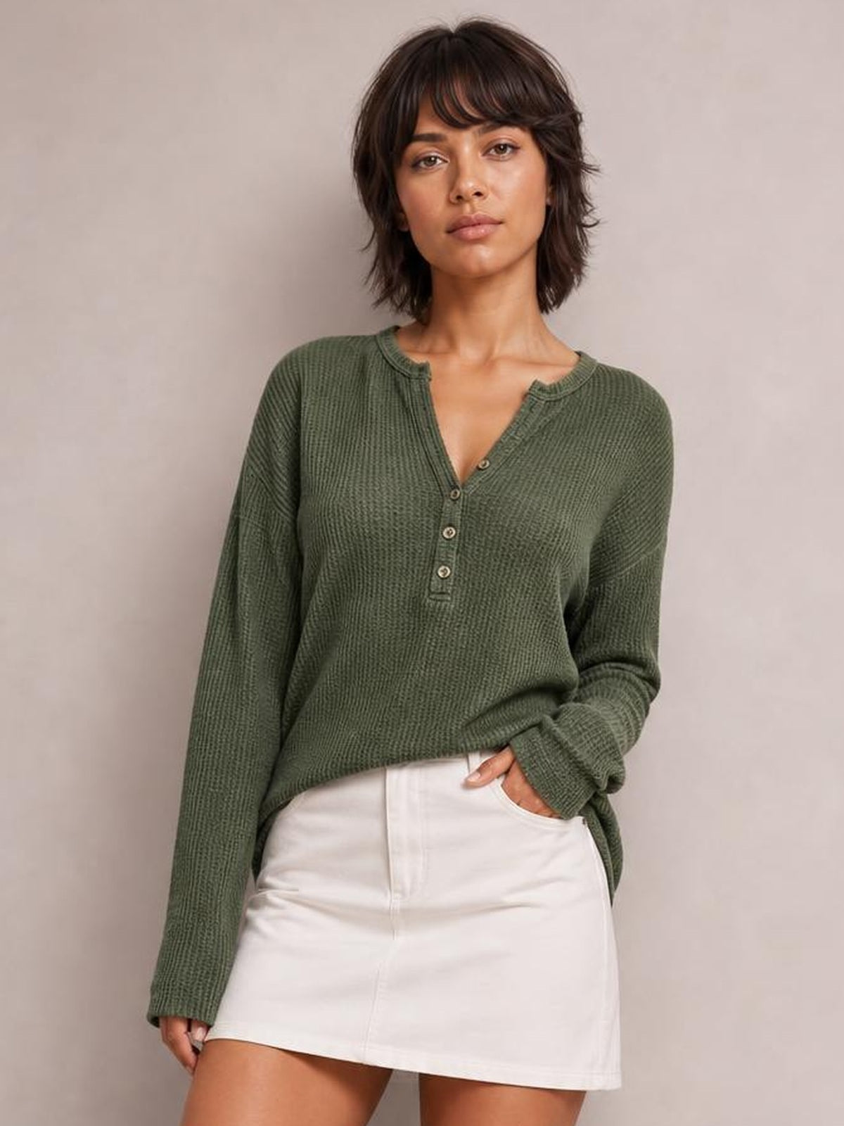 Model poses with one hand in a pocket wearing an olive-green long sleeve T-shirt with a notched neckline, buttoned placket, textured knit, and relaxed silhouette.