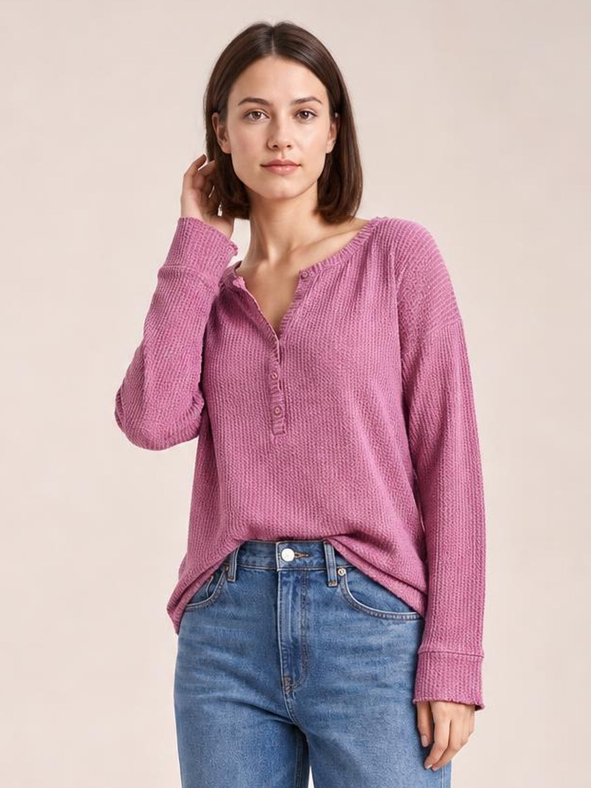 A model poses in a mauve pink long sleeve T-shirt with a relaxed silhouette, textured fabric, notched neckline, and button details.